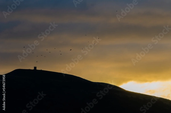 Fototapeta Birds flying over Rivington Pike at sunrise in Autumn Fall silhouette with motion blur