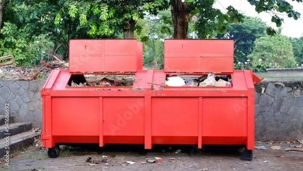 Fototapeta Metal durable orange industrial trash bin for outdoor trash at construction site. Large waste basket for household or industrial waste. A pile of waste