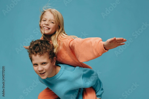 Fototapeta two happy friendly children, a boy and a girl, play and the brother rides his sister on his back. Themes of friendship and relationships between children