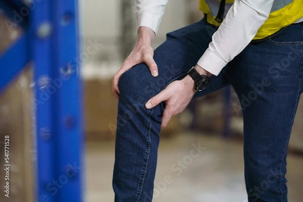 Fototapeta Factory worker has injured or pain at knee joint. Injury from working not properly in working place, Concept insurance for people that on duty in warehouse industrial.