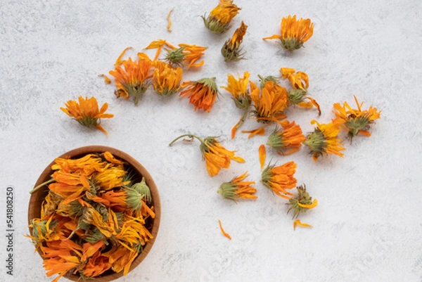 Fototapeta Orange and yellow calendula officinalis flowers in a wooden bowl on white background. Top view, copy space. Medicinal plant. Herbs harvesting, Drying and Storing Herbs. Marigold flowers on table