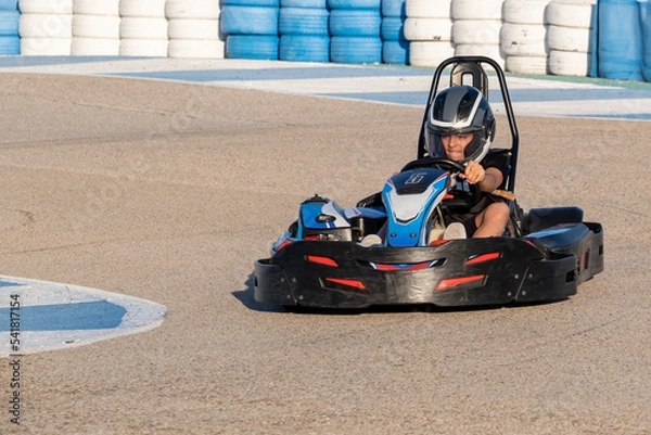 Obraz a teenager boy driving a kart at the exit of a curve of a karting circuit, face of speed and concentration while driving a go kart