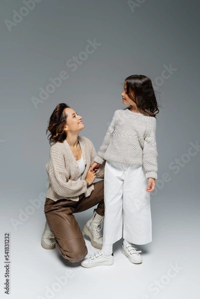 Fototapeta happy woman holding hand of stylish daughter on grey background
