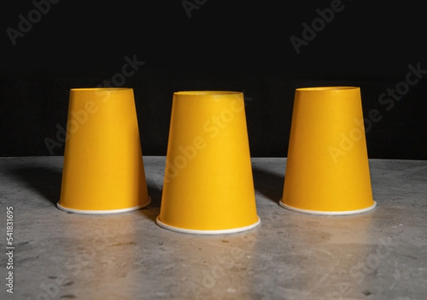 Obraz Three inverted yellow paper disposable cups. The concept of cheating, fraud, gambling.