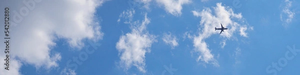 Fototapeta The passenger airplane is flying far away in the blue sky and white clouds. Plane in the air. International passenger air transportation. The airplane flies in the distance. Banner or header