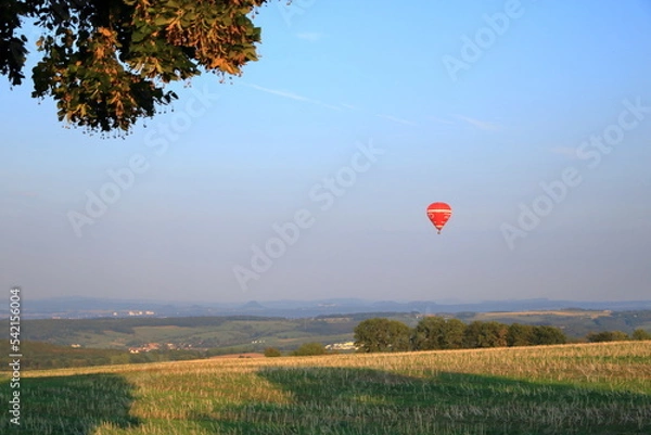 Fototapeta July 07 2022 - Saxony, Germany: A red hot-air balloon is landing in front of Saxon Switzerland