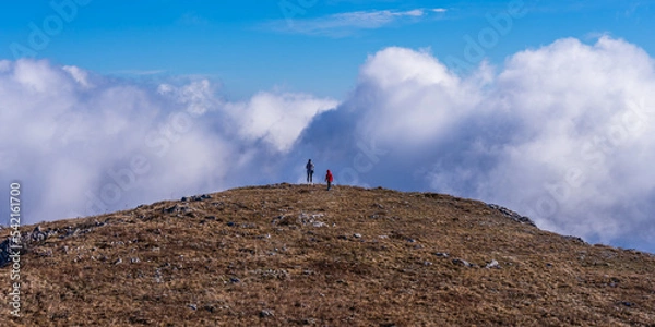 Obraz Mom and son are far away on the top of the mountain during a hike against the backdrop of clouds.