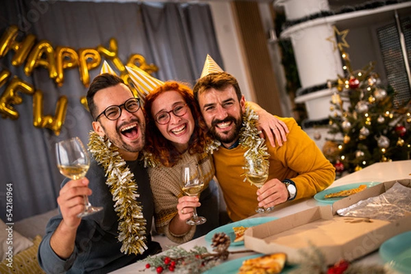 Fototapeta Young people looking at the camera smiling and laughing at the new year's party drinking wine and champagne.
