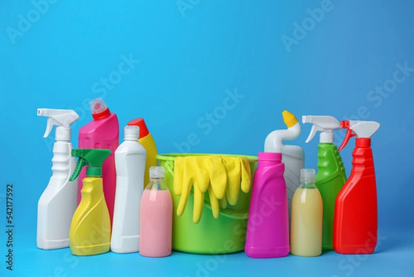 Fototapeta Green bucket, gloves and bottles of detergents on light blue background. Cleaning supplies