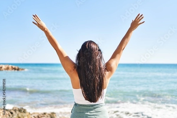 Fototapeta Young hispanic woman on back view with arms raised up at seaside