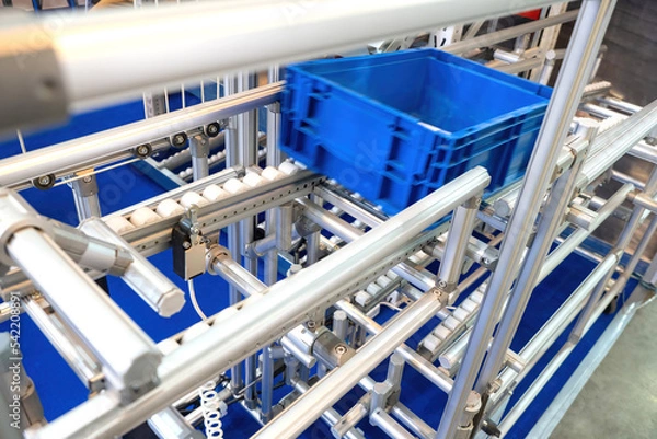 Fototapeta Modern production equipment. Blue box moves on steel rails. Fragment of production equipment. Modern production technologies. Empty box descends automatically. Production equipment without people