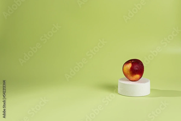Fototapeta On one white podium top hat there is a red apple, a green background and a shadow from sunlight