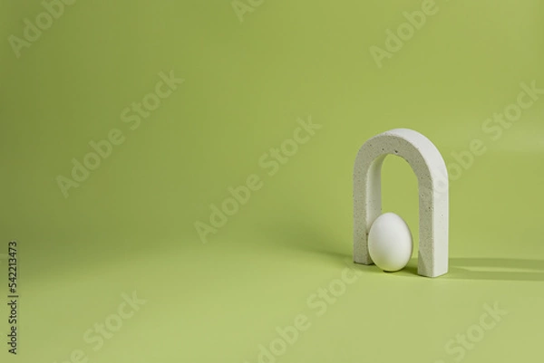 Fototapeta An empty stage with one white concrete arch under it, a white egg on a green background and a shadow from sunlight