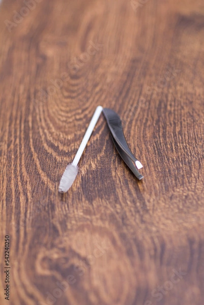 Fototapeta Silver tweezers for eyebrow correction and a white brush for combing eyebrows on a wooden table