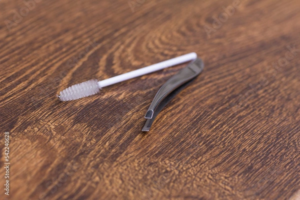 Fototapeta Silver tweezers for eyebrow correction and a white brush for combing eyebrows on a wooden table