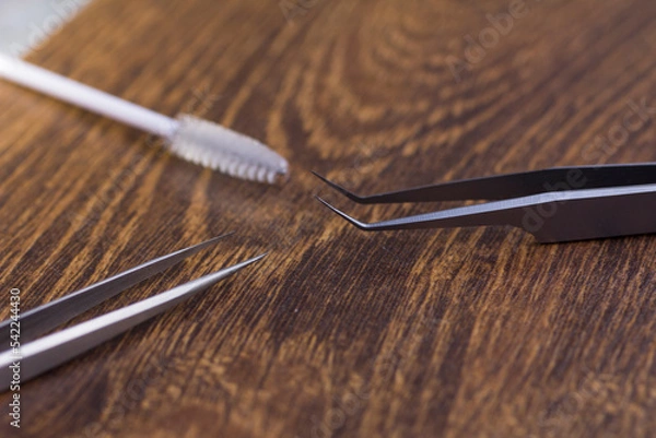 Fototapeta Sharp tweezers and eyelash extension brush on wooden background