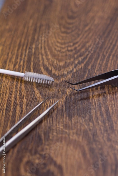 Fototapeta Sharp tweezers and eyelash extension brush on wooden background