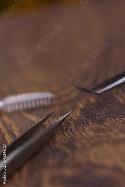 Fototapeta Sharp tweezers and eyelash extension brush on wooden background