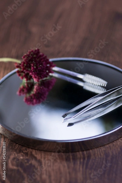 Fototapeta Eyebrow tweezers, brush and flower reflected on the mirror