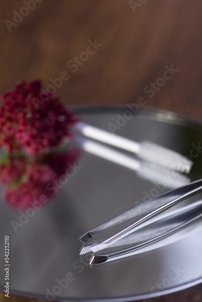 Fototapeta Eyebrow tweezers, brush and flower reflected on the mirror
