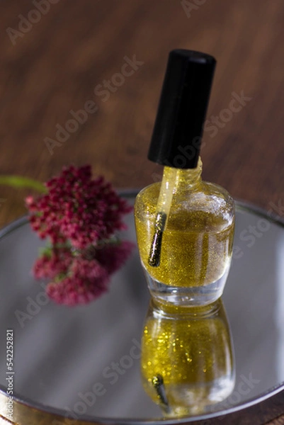 Fototapeta A translucent gold glitter nail polish with a rose red flower that reflects in the mirror.