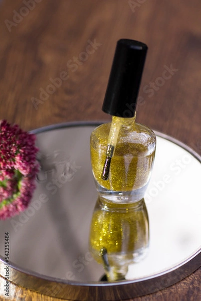 Fototapeta A translucent gold glitter nail polish with a rose red flower that reflects in the mirror.