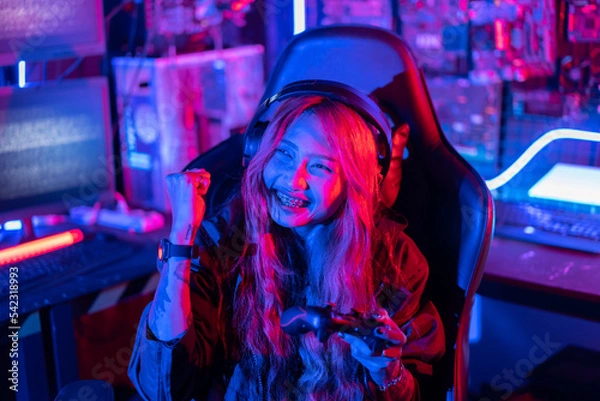 Fototapeta You win. Gamer using joystick controller plays online video game with computer neon lights backgrounds, woman use gaming headphones playing live stream esports games console at home.