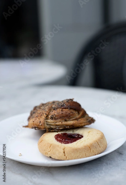 Fototapeta Classic Swedish shortbread cookie, known as hallongrotta, with jam in the middle and a cinnamon bun on a plate. Sweet pastry selection on plate on cafe table. Photo taken in Sweden.