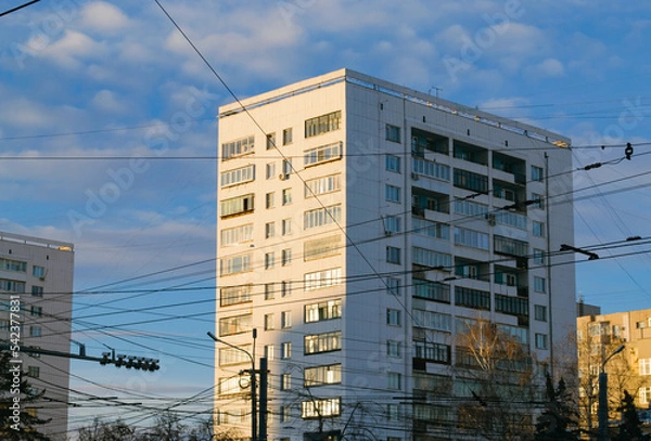 Obraz Close-up of a Soviet white high-rise building illuminated by the evening sun and many electrical wires in front of it against the blue sky