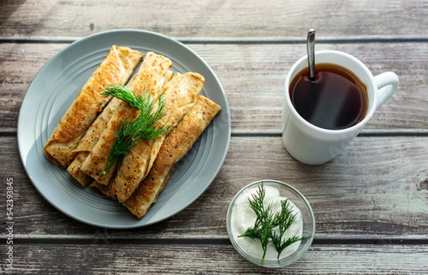Obraz Pancakes with meat on a gray plate, sour cream, garnished with dill. Tea in a white cup. wooden background