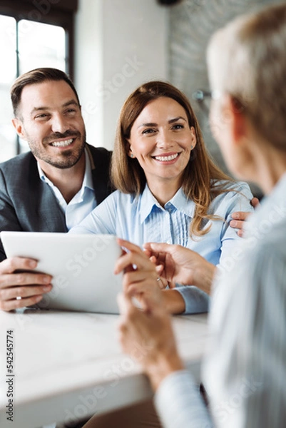 Fototapeta Happy couple using digital tablet while having a meeting with their insurance agent in the office