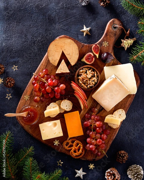 Fototapeta Christmas cheese platter with grapes, nuts, figs on a dark background. Top view. Xmas gourmet holiday appetizer. Copy space, top view.