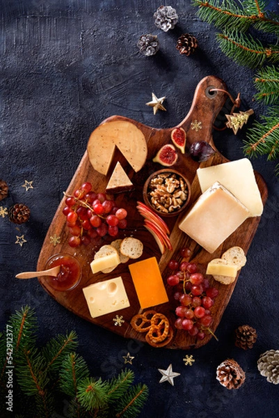 Obraz Christmas Cheese board appetizers platter with various types of cheese, crackers, jam, fruits, grape on a dark background. Overhead view, cope space.
