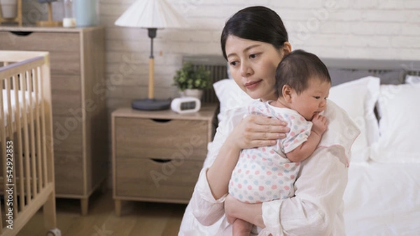 Obraz portrait asian mother is helping her adorable newborn to burp with gentle pat on the back in the bedroom at home.