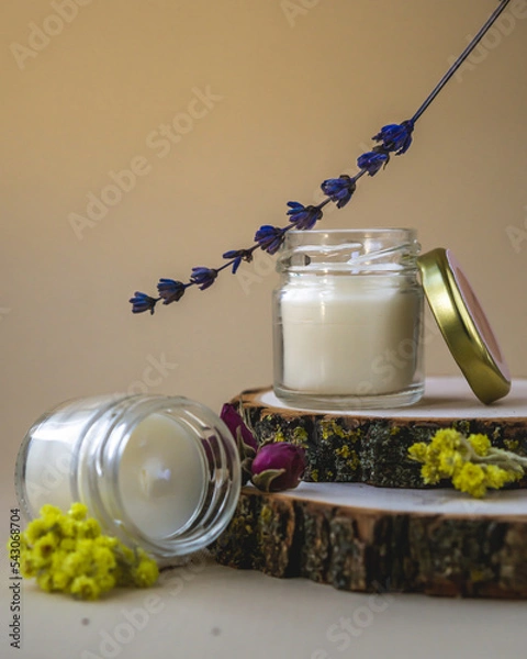 Fototapeta Wax candles in glass jars on wood stand. Set of natural soy wax scented candles withs herbs on beige background.