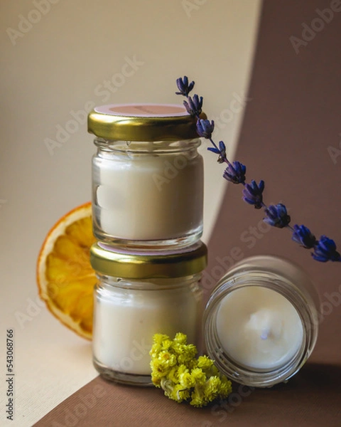 Fototapeta Wax candles in glass jars. Set of natural soy wax scented candles withs herbs on beige background.