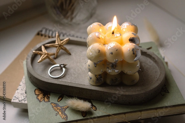 Fototapeta A square bubble candle is burning on a concrete stand. 