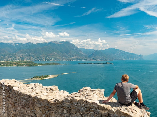 Fototapeta Boy sit  alone on rest of Manerba castle wall above Lago di Garda lake