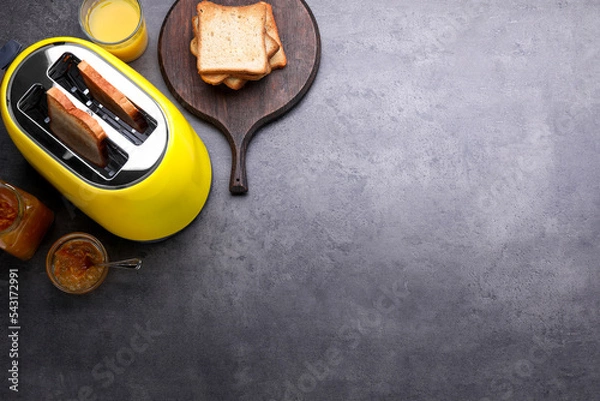 Fototapeta Yellow toaster with roasted bread, glass of juice and jam on grey table, flat lay. Space for text