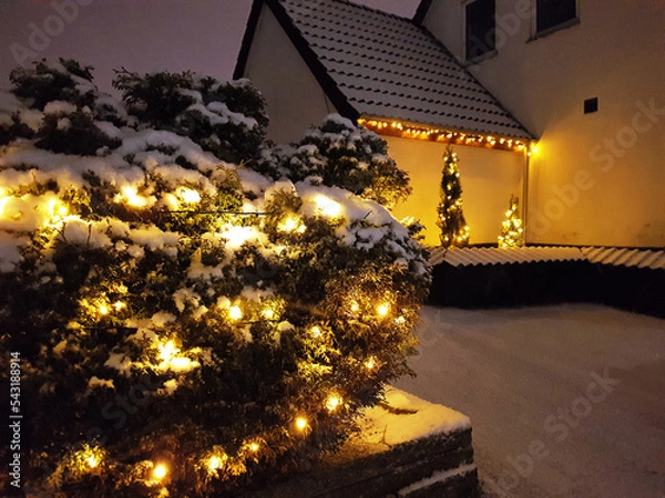 Fototapeta Danish home decorated with christmas lights glowing in the snow outside the house and in the garden in December