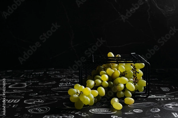 Fototapeta Kishmish grapes in a metal black grid stand, on a black background, in a low key, dark photo