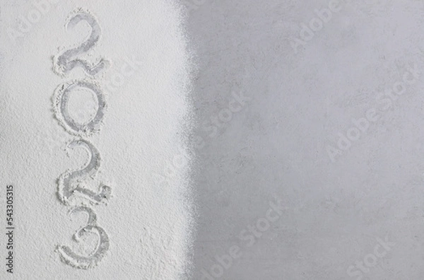 Fototapeta The numbers 2023 are handwritten on scattered flour on a gray stone surface. View from above. Concept: New Year and Christmas 2023. Copy space.