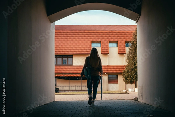 Fototapeta the silhouette of a girl walks through the tunnel from the arch of the house
