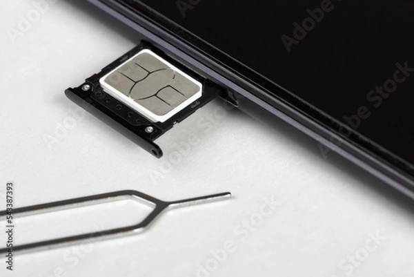 Obraz SIM card on the sim card tray of a smartphone on light background with pin needle tray remover