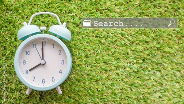 Obraz Alarm clock on green grass background with search bar and copy space.