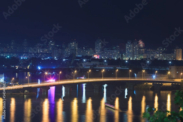 Fototapeta Car bridge over the river in a big city in a European city. Night landscape of a metropolis with a river, bridge and high-rise buildings.