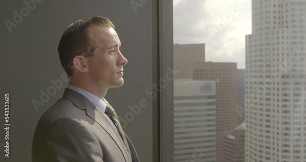 Fototapeta Successful, confident young business man looks across Los Angeles city skyline from Downtown office window.  Medium close up with sunrise sky 