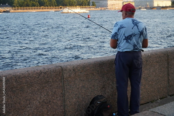 Fototapeta Saint Petersburg, Russia - August 19, 2022: A fisherman with a fishing rod on the embankment of the river Neva St. Petersburg