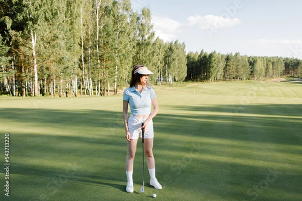 Fototapeta A woman plays golf on a green field in a golf club. Makes a kick to the ball. High quality photo