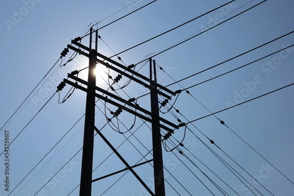 Fototapeta Silhouette of twin electric poles. Dark shadow of concrete power pole paired with high voltage cable with insulator and Guy Wire pulling pole on clear sky background with afternoon sun shining with co